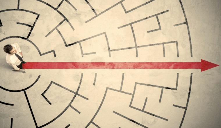 Business person standing in the middle of a circular maze with red arrow