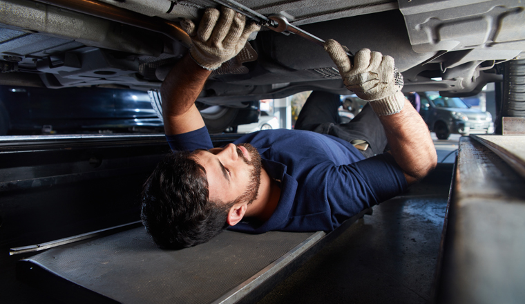 KFZ Mechaniker oder Mechatroniker kontrolliert Unterbodenschutz von Auto auf Rost